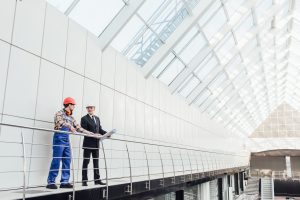 Standing industrial engineers in blue vests and helmets. Glass roof.